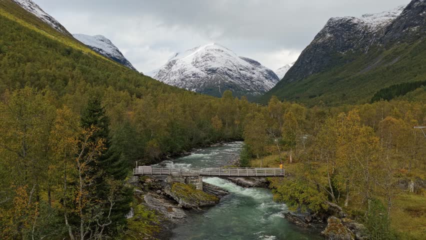 Man crossing a rustic bridge surrounded by mountain and river, Norway, Aerial