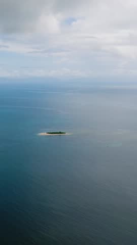 View of small island near green coastline surrounded by calm blue sea. Siargao, Philippines.