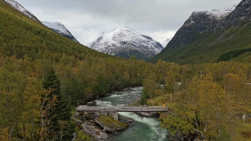 Person walking across a wooden footbridge over a river in scenic Norway, Aerial