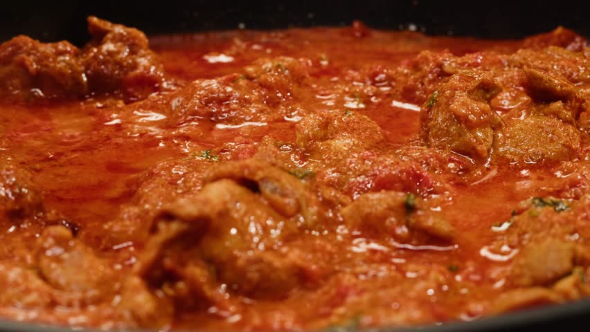 Cooking chicken Indian curry, tikka masala, chicken, lamb, mutton Rogan Josh grill boiling on pan, sauce. Dark background. Close up.