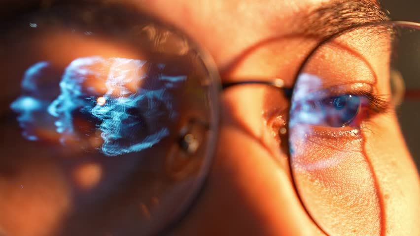 A close-up of a person wearing glasses while using a laptop, with a digital human face mesh reflected in the lenses, symbolizing AI technology, data analysis, and advanced digital intelligence.
