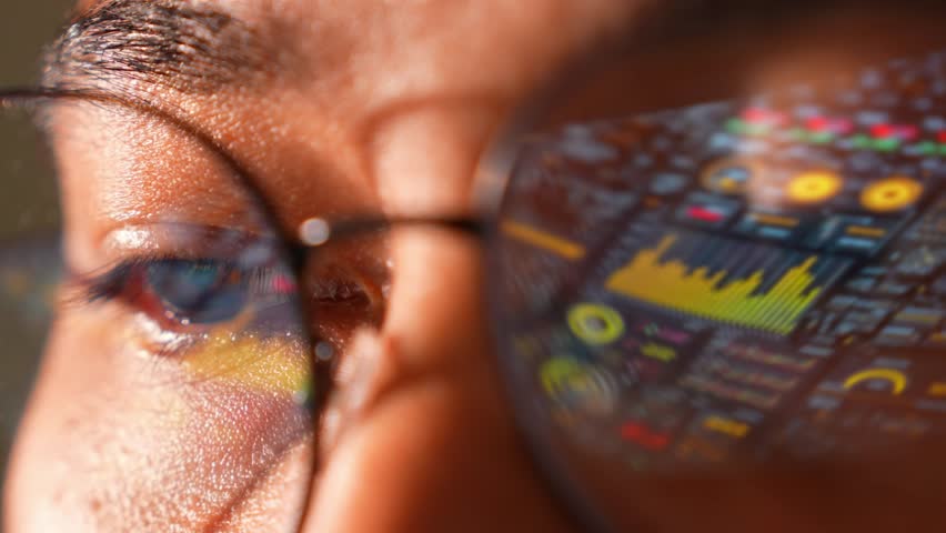 A person in glasses uses a laptop, a real-time data interface reflected signifying analytics, innovation, focus, digital transformation, decision-making, problem-solving, and agility.
