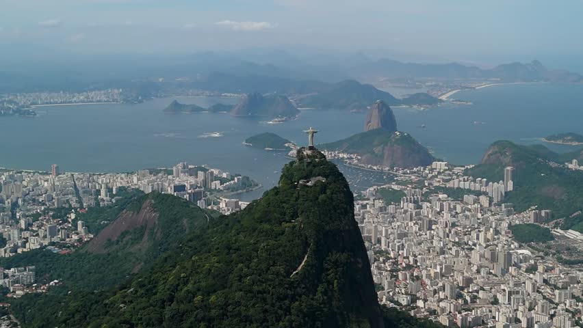 Aerial slow orbit circles Christ the Redeemer above the dense urban landscape of Rio de Janeiro