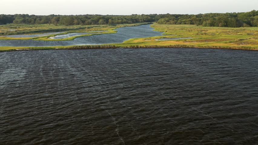 Descending crane shot over the waters at East Islip Marina - Park focusing on the marsh area with a wider chanel waterway on the left at sunset 4k