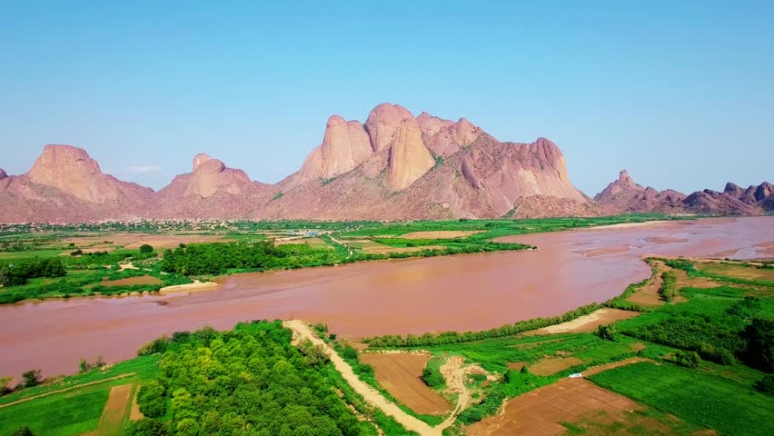Cinematic aerial footage of rugged mountain landscapes in West Sudan, featuring rocky peaks, natural terrain, and vast open horizons under clear daylight. The scene highlights untouched geography and remote wilderness beauty. Filmed on 10 December 2025.