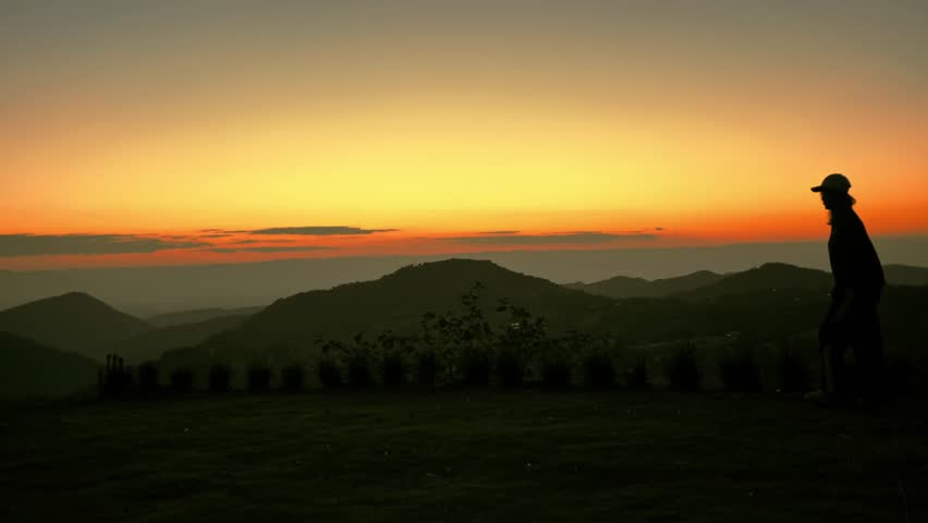 A silhouette of a men walking and admiring the mountain view during a dramatic sunset. This peaceful outdoor scene captures a sense of freedom and inspiration in the beautiful wilderness at dusk.