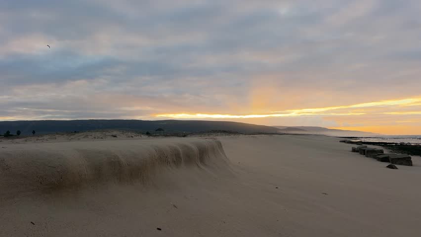 Time lapse of a serene coastal landscape at sunset with extensive sand dunes in the foreground.
