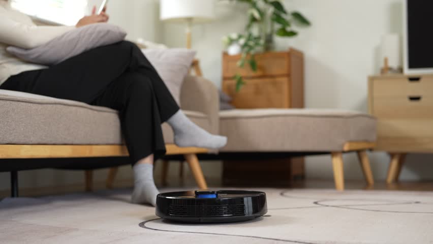 Young woman turning on robot vacuum cleaner from her smartphone to do housework