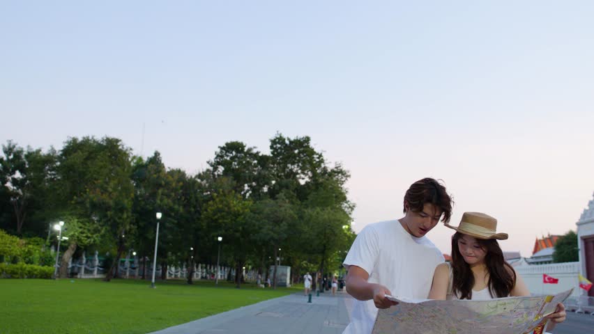 Tourist couple studies paper map near ornate temple at sunset, handheld medium shot