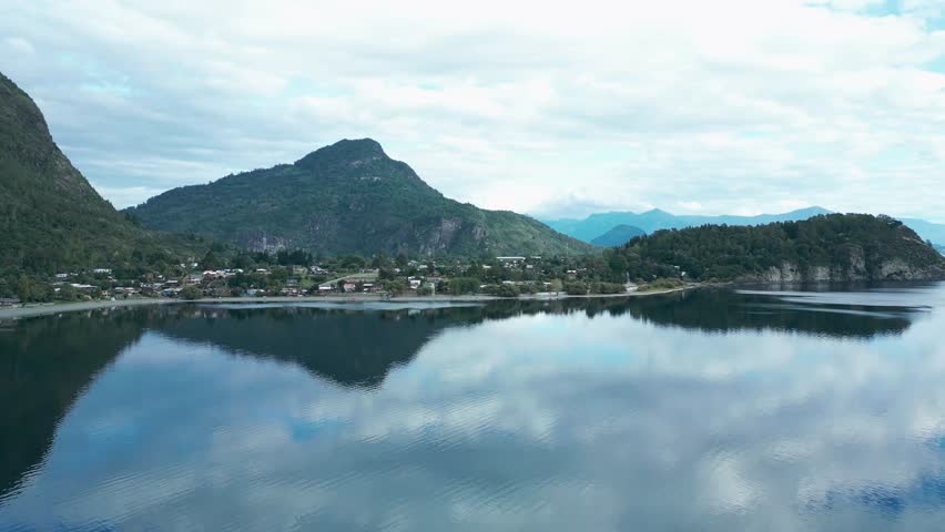 Forward drone aerial of Llifen town on Ranco Lake with mirror reflections, mountains backdrop, and serene Chilean wilderness panorama