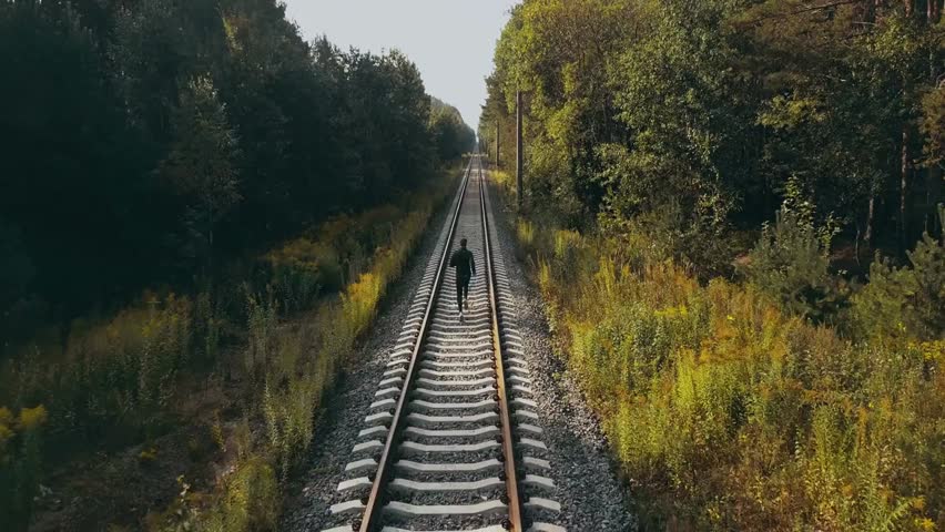Drone back view of a man running on an autumn forest railroad, capturing athletic motion, cinematic perspective, and the journey toward a clear horizon.