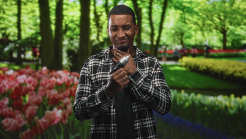 Man holding electric screwdriver, touching neck while wincing in a forest tulip garden; discomfort safety.