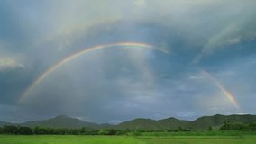 This 4K footage captures a magnificent double rainbow, a rare optical phenomenon featuring two concentric arcs across the sky. The video clearly illustrates the scientific distinction between the two: the primary, inner rainbow is formed by a single reflection of sunlight within raindrops, while the fainter secondary arc is created by a double reflection. A key detail highlighted in this high-resolution shot is the color inversion between the two bands; the primary rainbow displays red on the outer edge, whereas the secondary arc shows red on the inside. Set against a dramatic, post-storm sky, this sequence serves as a perfect visual for atmospheric science, meteorology, and natural wonders. The crisp detail and vibrant spectrum make it ideal for educational content or as a serene, cinematic backdrop. - Powered by Shutterstock - Get 15% off with code: PIKWIZARD15