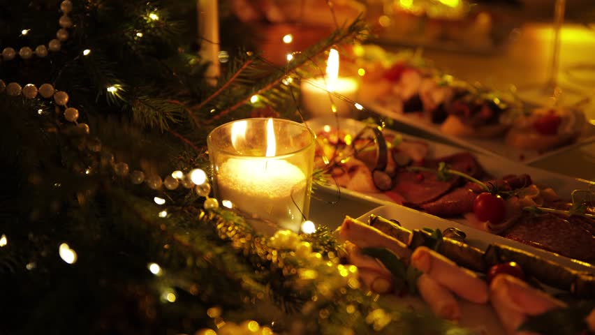A table with beautiful food decorated with Christmas tree branches and garlands. A festive table with food, drinks, and decorations made of Christmas tree branches and glowing lanterns.