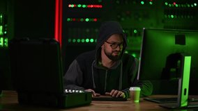Young man in a hoodie programming in a server room. Malicious programmer developing malware or breaching cybersecurity in a dark environment - Powered by Shutterstock - Get 15% off with code: PIKWIZARD15