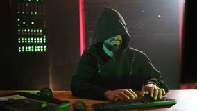 Mysterious hooded computer programmer working in a dark server room. Anonymous male hacker coding a virus, developing malware, or breaching a data system - Powered by Shutterstock - Get 15% off with code: PIKWIZARD15