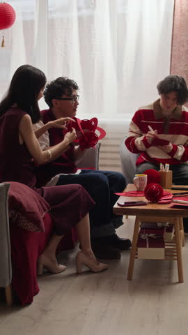 Vertical shot of group of young Asian friends making red decorations while celebrating Tet together at home
