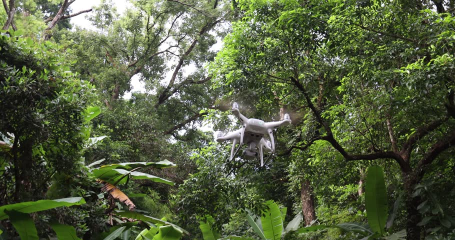 Aerial footage of a white drone flying in beautiful tropical forest  