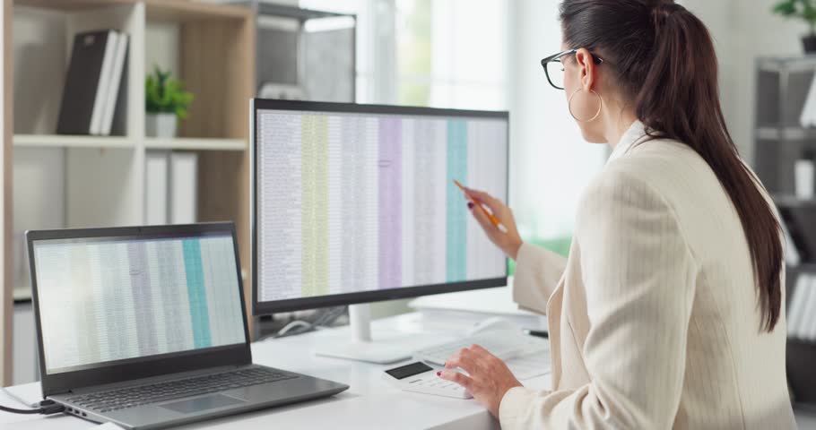 Auditor woman accountant in office reviewing finance. She checks spreadsheet data on computer monitors for analysis, bookkeeping, reporting and compliance. Clear finance audit concept theme.