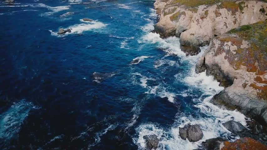 Aerial view of stunning ocean shoreline at Big Sur, California, with powerful waves crashing over rocky cliffs, showcasing dramatic coastal nature and scenery.