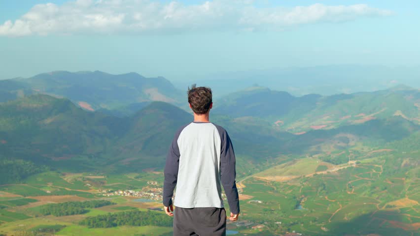 Man seen from behind with his arms open, expressing gratitude and happiness for his success while admiring a beautiful mountain landscape in the background