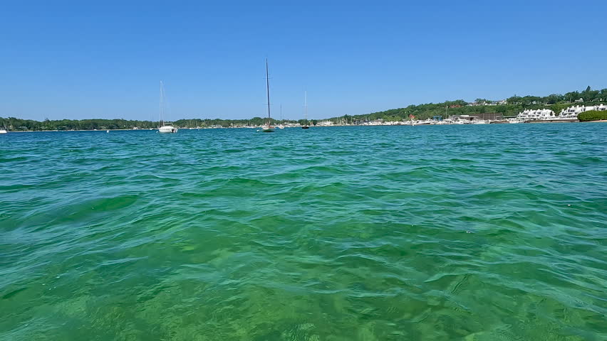 Beautiful Boats in the Marina on Lake Michigan. Surface level views of the crystal clear lake water in a bay on Lake Michigan in Northern Michigan, USA. Sailboats and yachts are moored in the bay of water.