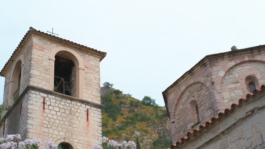 Medieval stone bell tower in kotor montenegro. Ancient stone bell tower of a christian church surrounded by lush pink oleander flowers and green mountains in the historic old town of kotor, montenegro