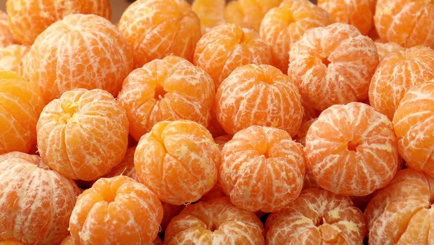 Woman peeling tangerine among many peeled tangerines, closeup