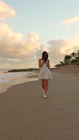 Woman in white dress walking along beach at sunset in West Palm Beach