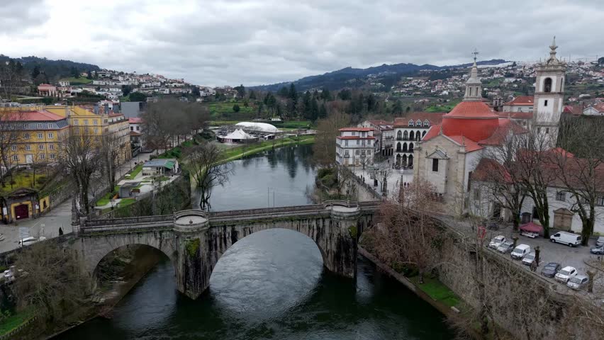 Historic St Goncalo stone bridge over Tamega River connecting Sao Goncalo catholic church area, Amarante city landscape, Aerial pullback shot