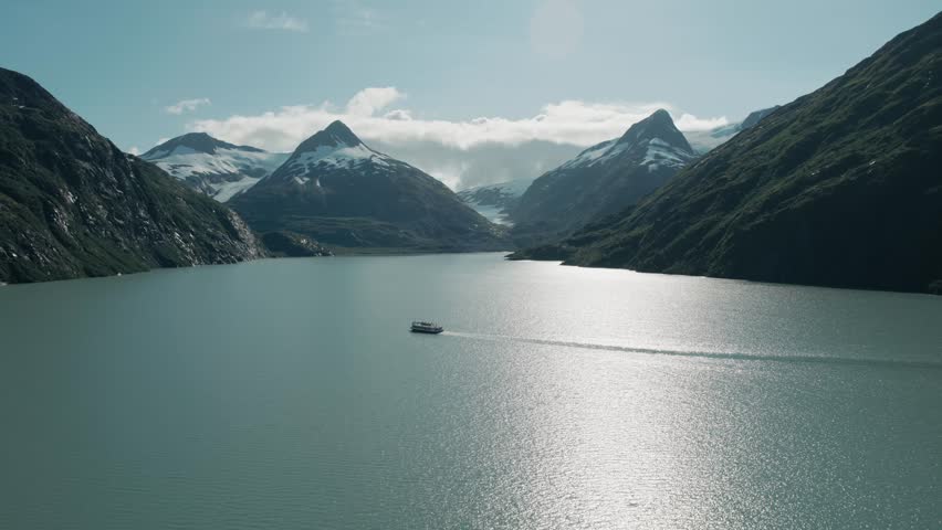 Pull out aerial shot of the mountains of Alaska with a guide boat in frame.