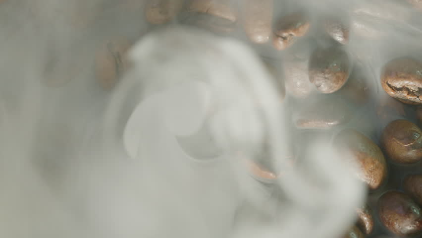 Roasting coffee beans with smoke against a dark background. Smoke emanates from fresh coffee beans.
