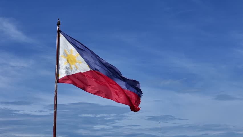 Philippine flag waving in the wind against a clear blue sky. Outdoor scene highlights fabric texture, natural movement, and national symbolism.