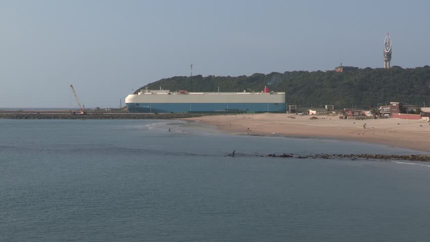 A wide shot of  a large cargo ship leaving Durban  harbour  / harbor at mid-day 