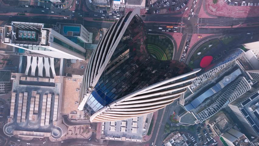 Straight-down drone over a ribbed skyscraper complex in Kuwait City: glass teardrop forms, landscaped tiers and a dense street grid with traffic—crisp architecture b-roll for business and editorial.