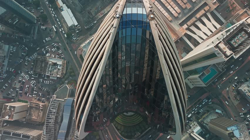 Straight-down drone over a ribbed skyscraper in Kuwait City glass crown, sculpted fins and landscaped tiers framed by busy streets, parking and towers crisp architecture b-roll for business editorial