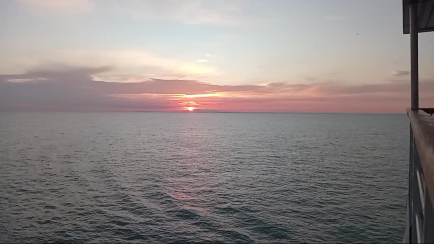 Stunning sunset timelapse from a luxury yacht deck at sea. Golden hour light reflecting on calm ocean waves during a peaceful nautical voyage. High-end travel, summer vacation, and serene escape.