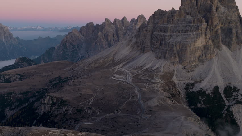 Cinematic aerial view of the Dolomites in Italy, rugged alpine peaks glowing at dawn, dramatic cliffs and deep shadowed valleys creating a serene high-altitude mood