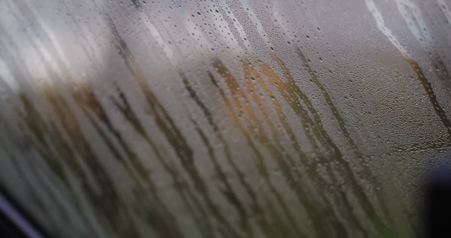 Close‑up shot of condensed water droplets streaming down the inside of a camper van window on a cold, damp day, forming vertical streaks on the glass with blurred outdoors beyond.
