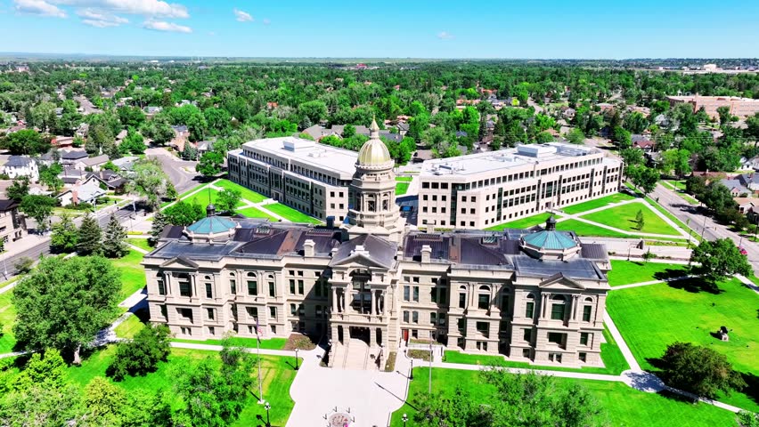 Aerial orbit of the Wyoming State Capitol building in Cheyenne on a clear summer day, captured on 16 June 2025. Smooth drone motion reveals the historic dome, surrounding city streets, green lawns, and vibrant state capital atmosphere.