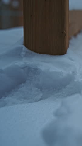 Fresh snow forming a thick layer on an outdoor residential railing with soft background blur and calm atmosphere. Vertical format. Lateral movement.