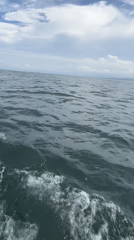 Close up of sea waves with white foam from a moving boat under a cloudy blue sky”