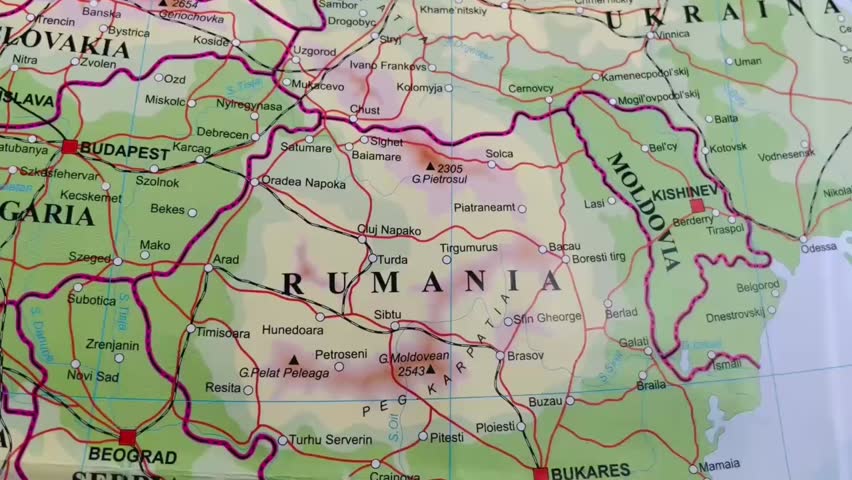 Close-up footage of a printed political map of Romania, highlighting country borders, major cities, roads, and neighboring countries. The camera focuses on Romania’s geographic location in Eastern Europe, with visible labels such as Bucharest and surrounding regions. Ideal for use in educational content, travel videos, geopolitical analysis, news reports, documentaries, and historical or geographic presentations.