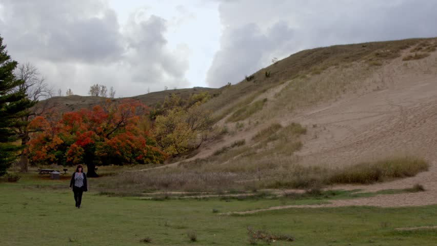Middle aged woman walking near the Dune Climb at the Sleeping Bear Dunes National Lakeshore in Michigan on an autumn day with stable video.