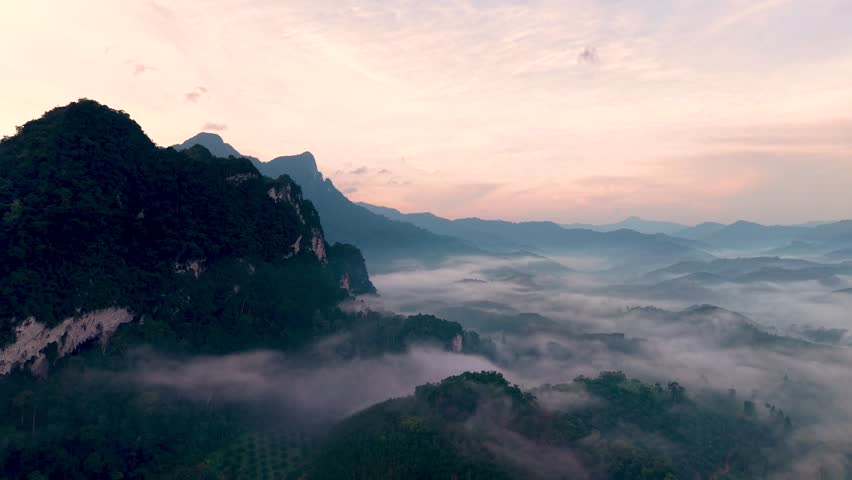 Explore the stunning beauty of Khao Sok in Thailand as mist blankets the lush mountains at dawn. Nature awakens, revealing vibrant greenery and dramatic cliffs in a tranquil atmosphere.