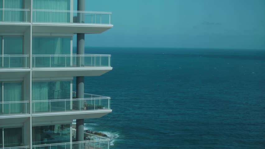 Static shot of modern apartment balconies facing the Mediterranean Sea along the Maltese coastline, showing open water and contemporary seaside architecture.