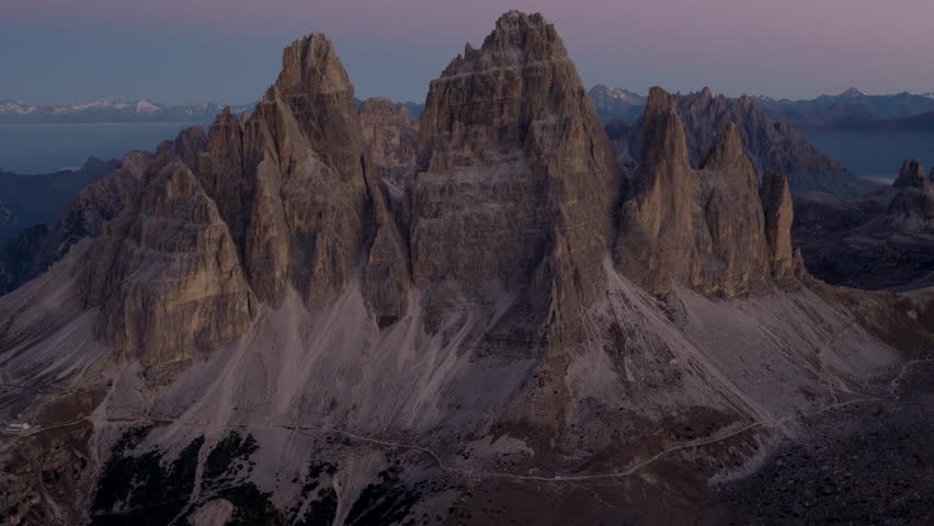 Cinematic aerial view of the Dolomites in Italy, rugged alpine peaks glowing at dawn, dramatic cliffs and deep shadowed valleys creating a serene high-altitude mood