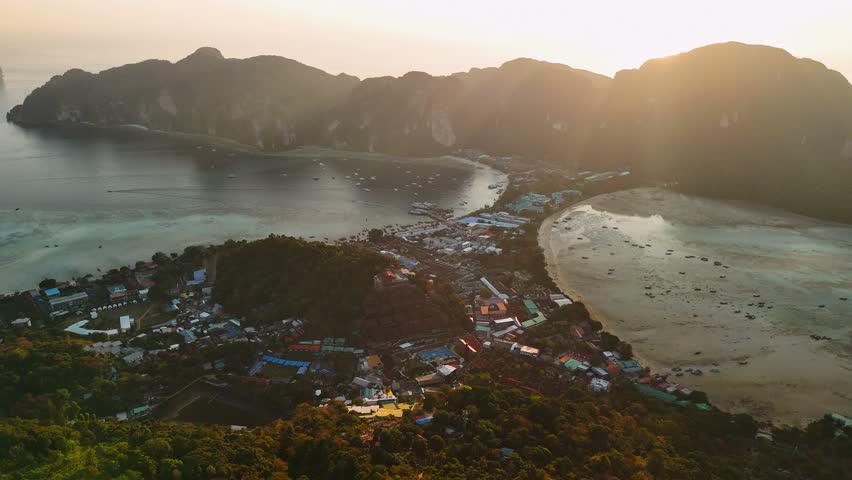 Golden sunset illuminating phi phi islands tropical coastline, revealing vibrant village nestled between azure waters and verdant landscape in thai archipelago, Thailand