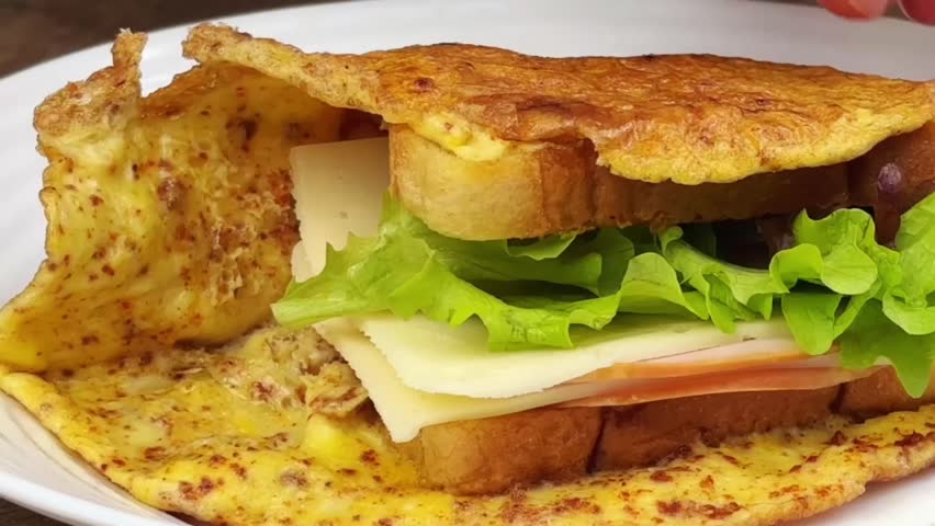 Cutting a stuffed egg omelette sandwich with a knife to show the fresh layers