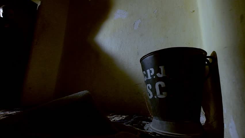 A prisoner is entering an old prison cell, while the door is casting interesting shadows on the walls. on the floor there